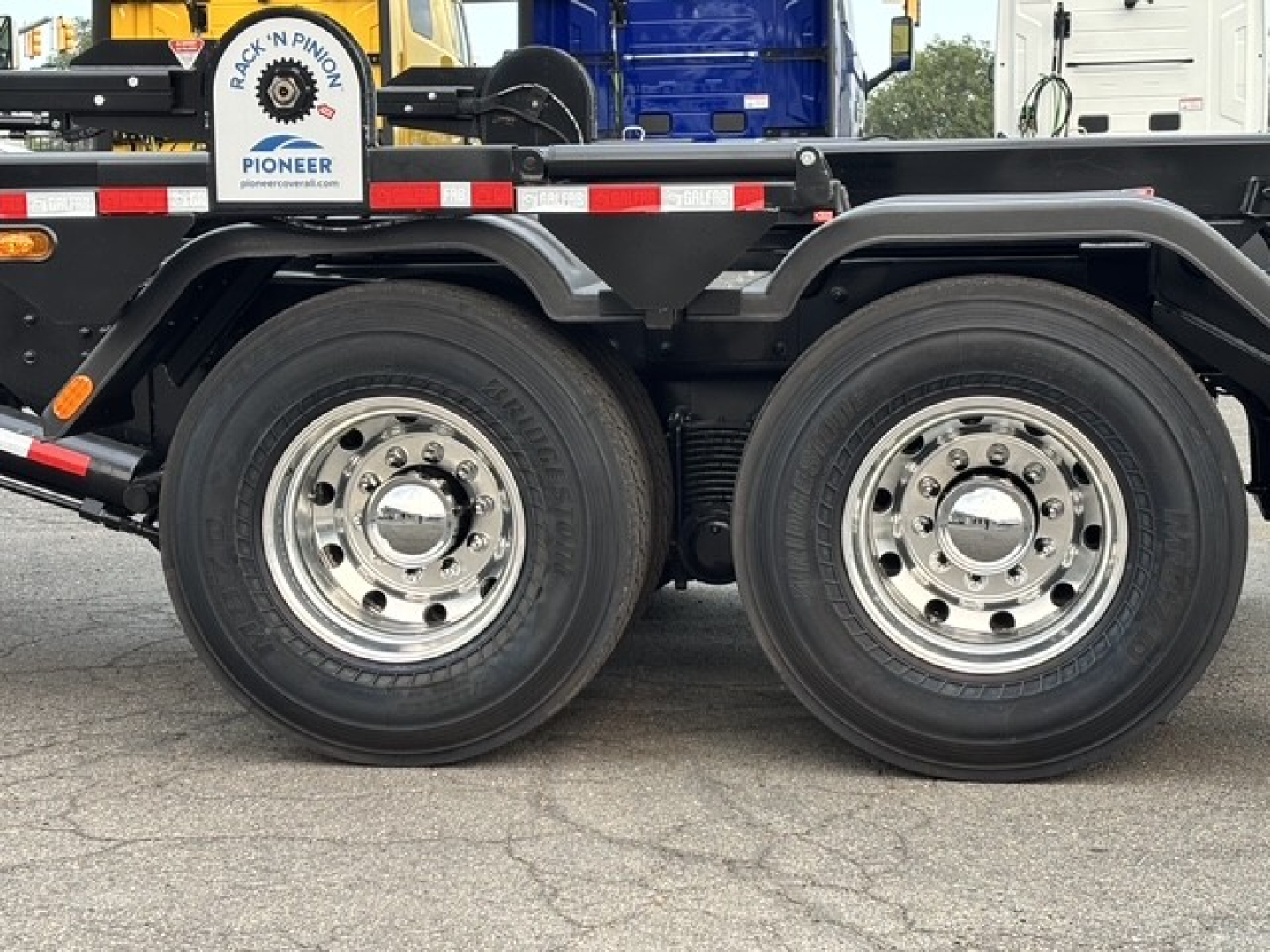 Two rear axles with polished wheels on a new Mack GR64B roll-off truck, black chassis with red-white reflective stripes.
