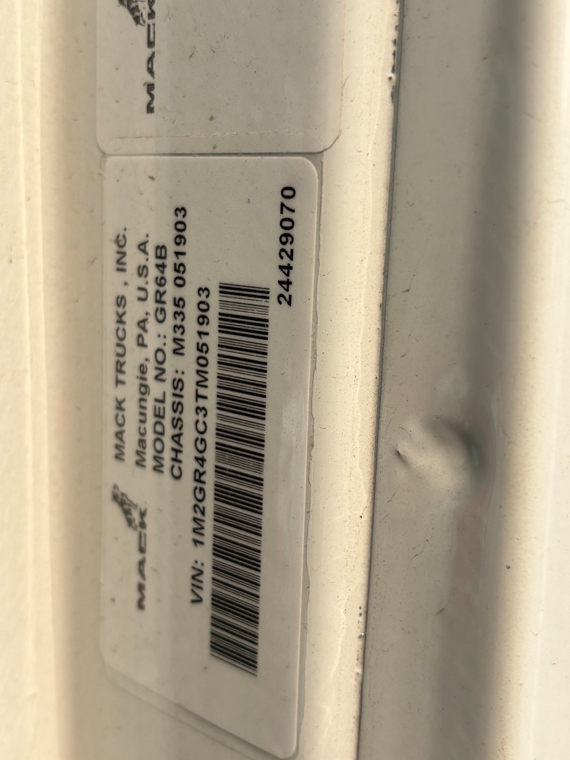 Label on Mack truck door frame showing MACK TRUCKS INC, MODEL GR64S? or GR64? with VIN 1M2GR4GC3TM051903 and stock 691?003; barcode; other text rotated.