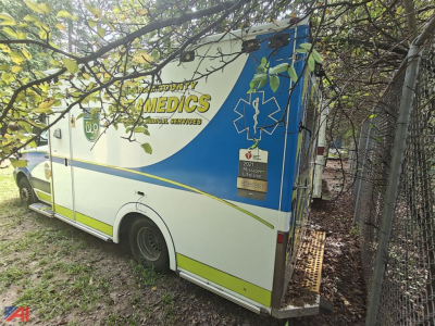 Ambulance side rear view showing Mercedes Sprinter ambulance with blue medical graphics, emergency medical services label, rear door, and service stickers.