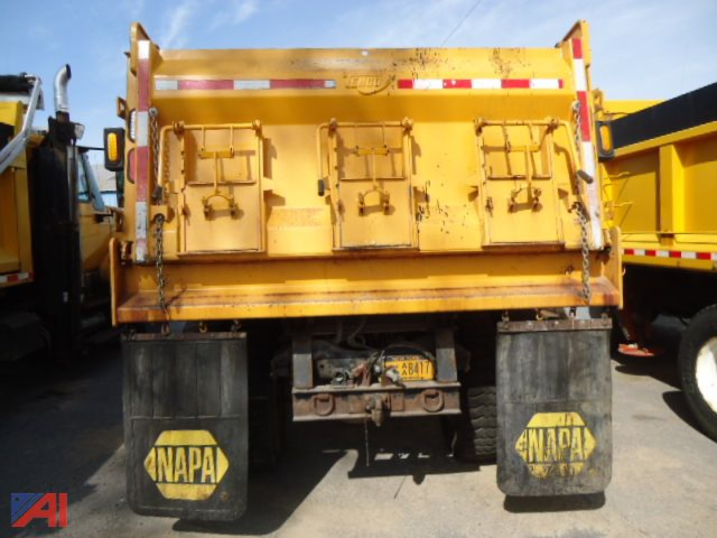 Rear of a yellow 1995 Ford L8000 dump truck showing dump bed, taillights, bumper, and dual rear wheels with ANAPA mud flaps.