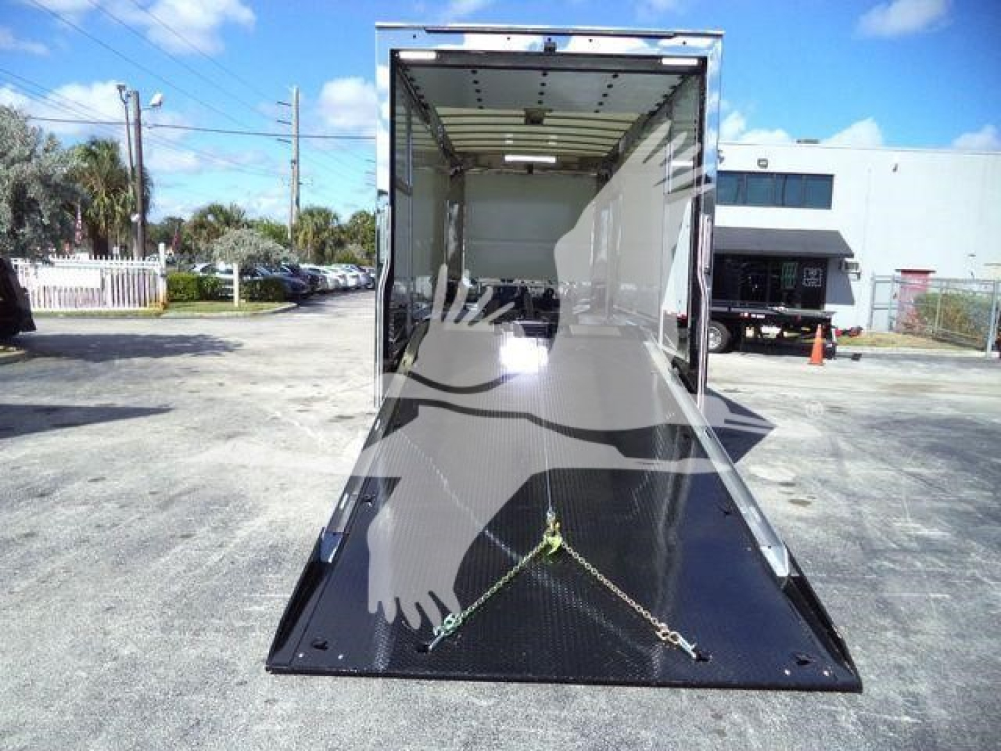 Open 28-foot rollback truck with ramp extended, interior white walls, black perforated metal ramp, chains securing load, outdoor dealership lot.