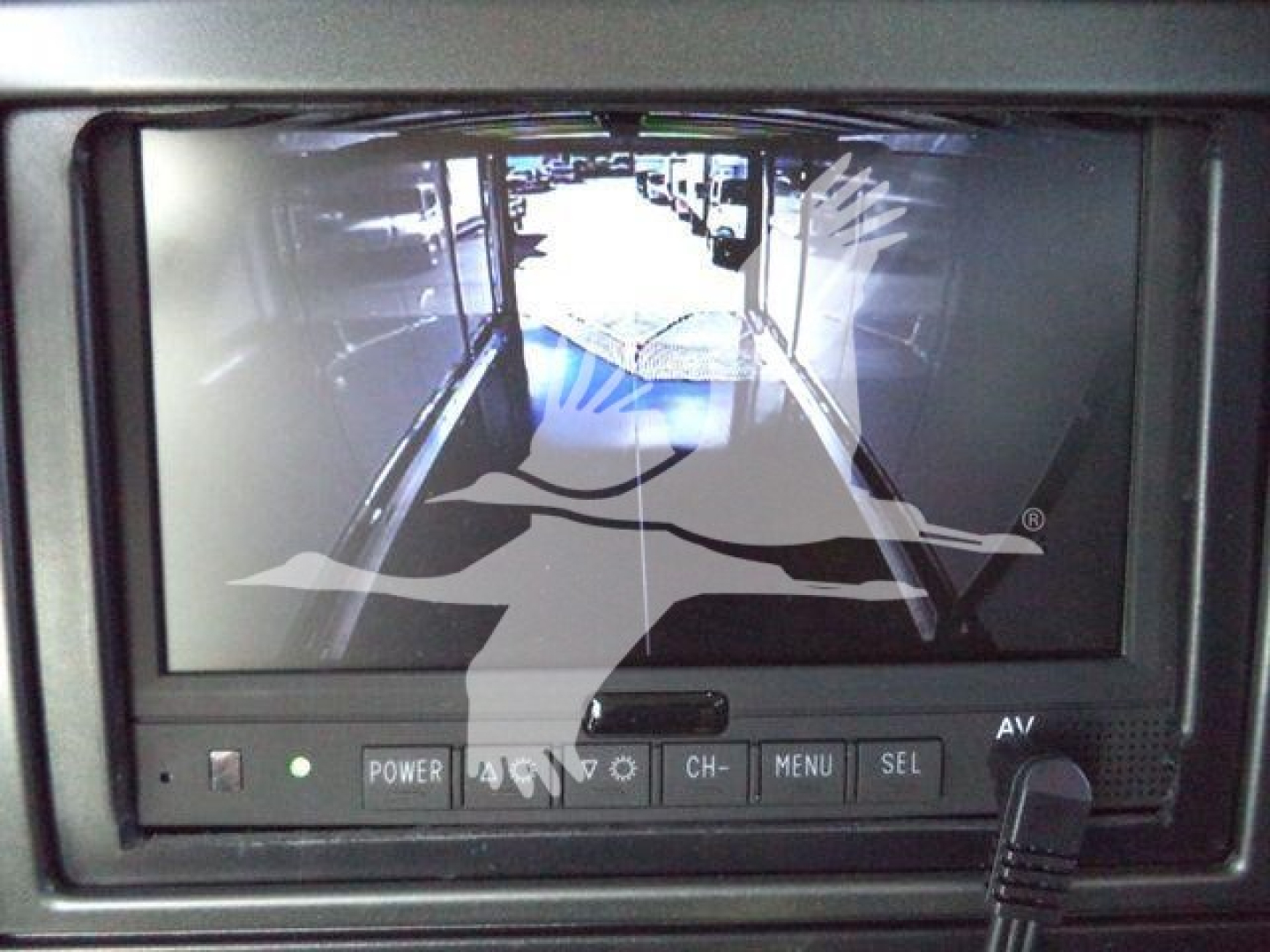 In-vehicle display showing a camera feed from a Mack MD6 rollback truck, with control buttons labeled POWER AV, CH, MENU, SEL, and a joystick-style knob.