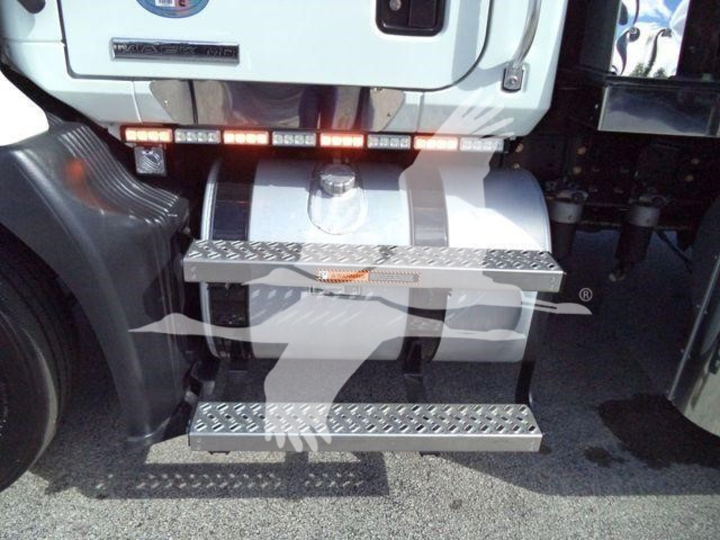 Rear view of a Mack MD6 rollback truck showing diamond plate steps and bumper, with a storage box and taillight strip.