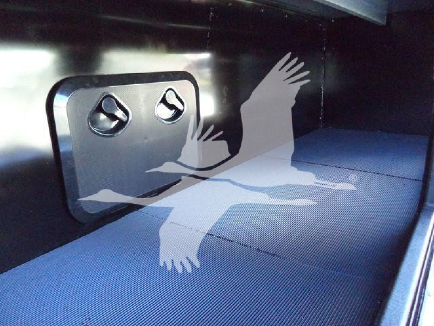 Interior of a Mack MD6 rollback truck showing a blue ribbed floor and a square access hatch with two circular latches.