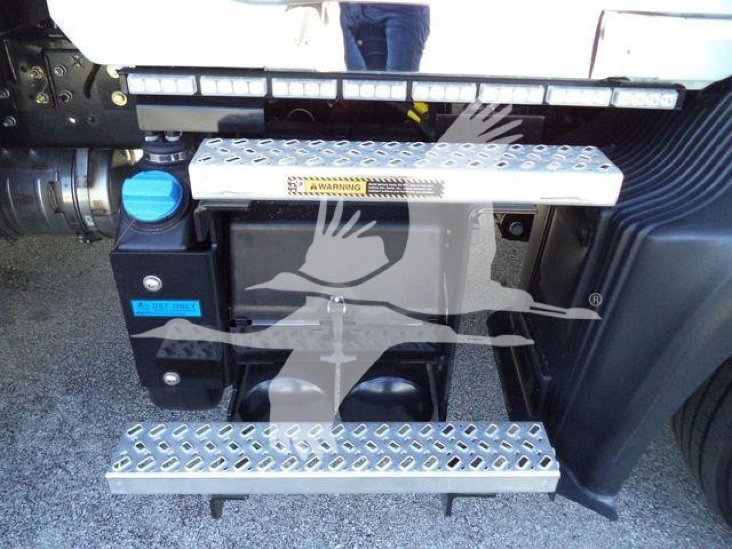 Step/footboard area of a Mack MD6 truck showing diamond plate running boards and a blue reservoir cap.