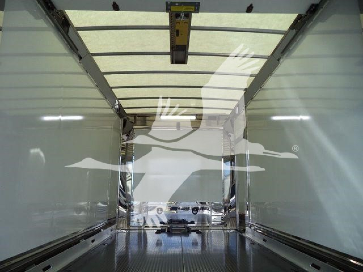 Truck trailer interior showing empty cargo area with side rails and ceiling track, reflection of exterior truck silhouette visible in rear opening.