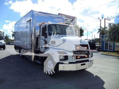 Front-right angle shot of a 2026 Mack MD6 rollback truck with large chrome bumper and aluminum cargo body, dealership lot in background.