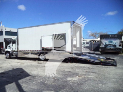 Truck with a rollback trailer attached to a white Mack MD6 cab and box, loading ramp deployed.