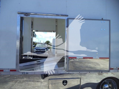 MD6 rollback truck trailer with rear swing-out access door open, showing cargo area and partial reflection of pickup truck in the background.