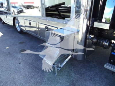 Side view of a 2026 Mack MD6 rollback truck showing a metal step/storage box attached to the side, chrome trim, and polished panels.