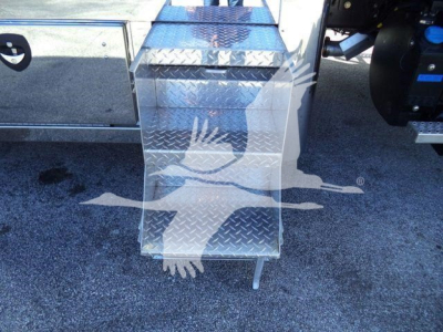 Aluminum diamond-plate stair step with step treads on a truck, part of a Mack MD6 rollback unit; visible tread pattern and a blue hydraulic reservoir cap on right.