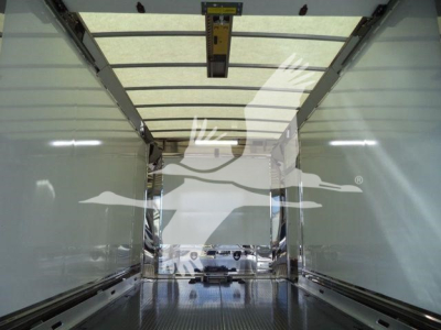 Truck trailer interior showing empty cargo area with side rails and ceiling track, reflection of exterior truck silhouette visible in rear opening.
