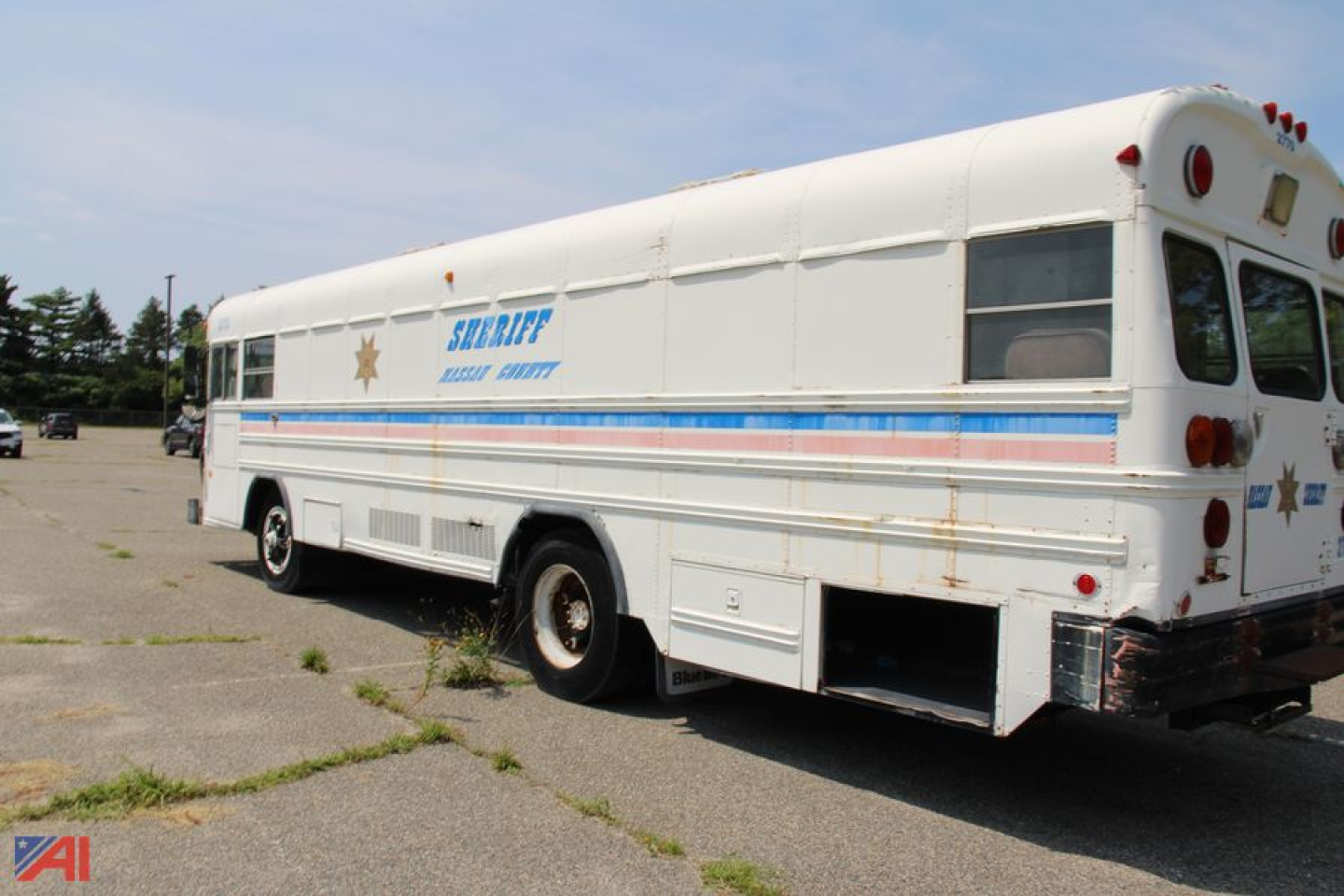 Bus side and rear view showing a bluebird school bus style with Sheriff banner and stripes along the side. Visible text includes SHERIFF and a blue stripe with orange accent.