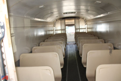 Bus interior showing seating arrangement in a 1995 Blue Bird TC2000 school bus converted layout with tan seats and narrow aisle.