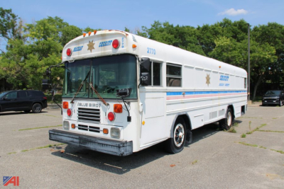 Blue Bird TC2000 school bus in white/blue livery with emergency lights and 'Blue Bird' branding visible.