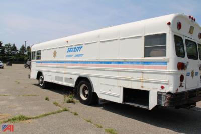 Bus side and rear view showing a bluebird school bus style with Sheriff banner and stripes along the side. Visible text includes SHERIFF and a blue stripe with orange accent.