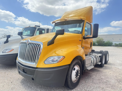 International LT truck in orange cab side view showing front grille, headlights, and dual rear axles with sleeper area raised