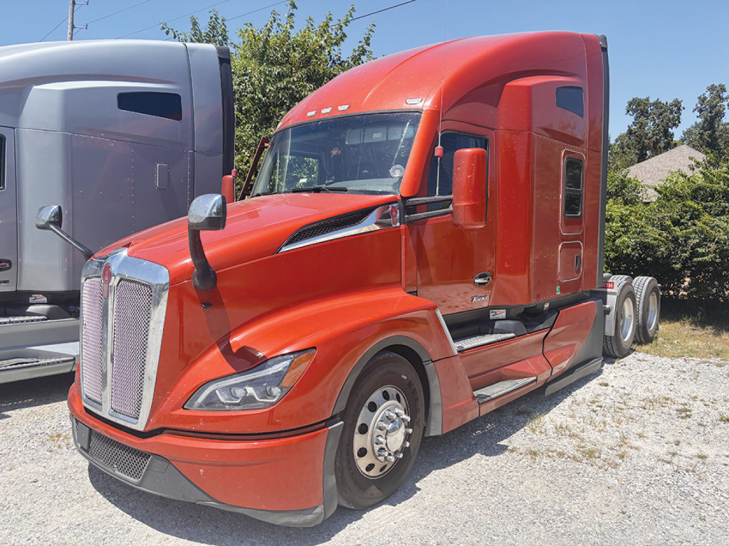 Kenworth T680 Next Gen tractor in red, front-left view, with sleeper cab and chrome grille, parked on gravel.
