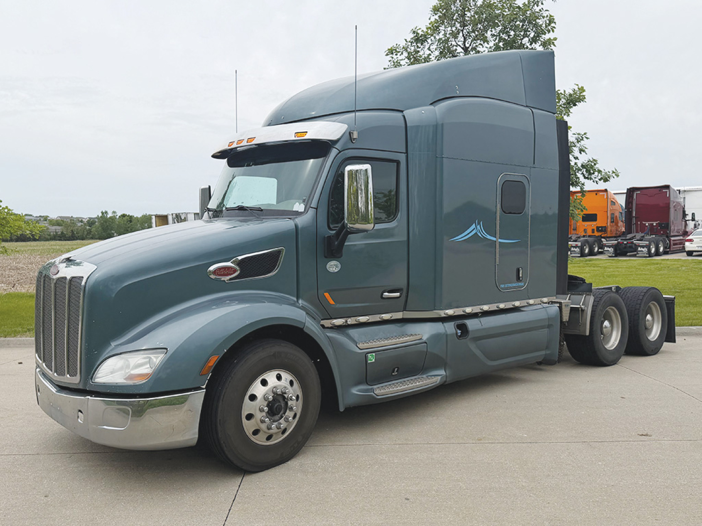 Peterbilt 579 UltraCab tractor in blue-gray, side view showing sleeper cab, chrome bumper, twin rear axles, and aerodynamic mirrors.