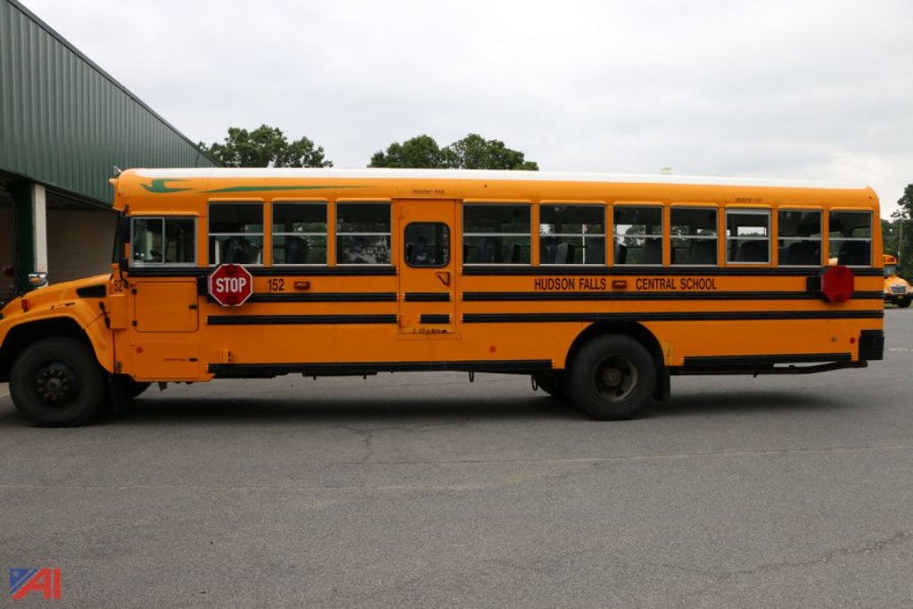 School bus side view showing yellow body, black striped accents, and stop sign; "HUDSON FALLS C CENTRAL SCHOOL" lettering near mid-section; blue bird logo on front; number 150 on stop sign.