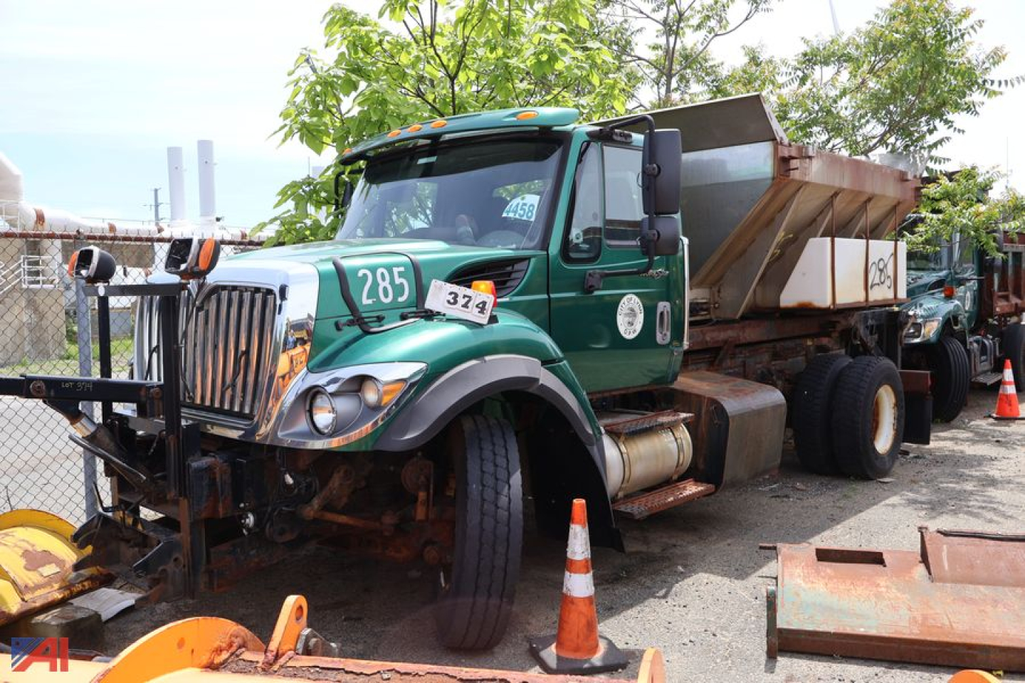 2013 International WorkStar 7400 Hookloader chassis with green cab and large dump bed, visible numbers 285 and 374 on the doors, front bumper guard, and orange traffic cones.