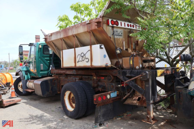 Dump body chassis showing hookloader undercarriage and rear tires with chains and support legs.