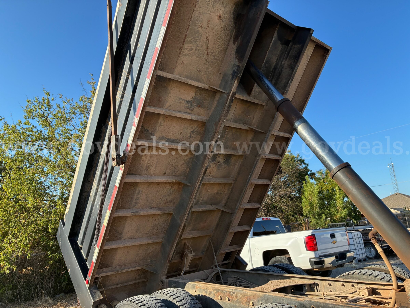 Dump truck bed raised showing hydraulic cylinder and underside of dump body with metal ribs.