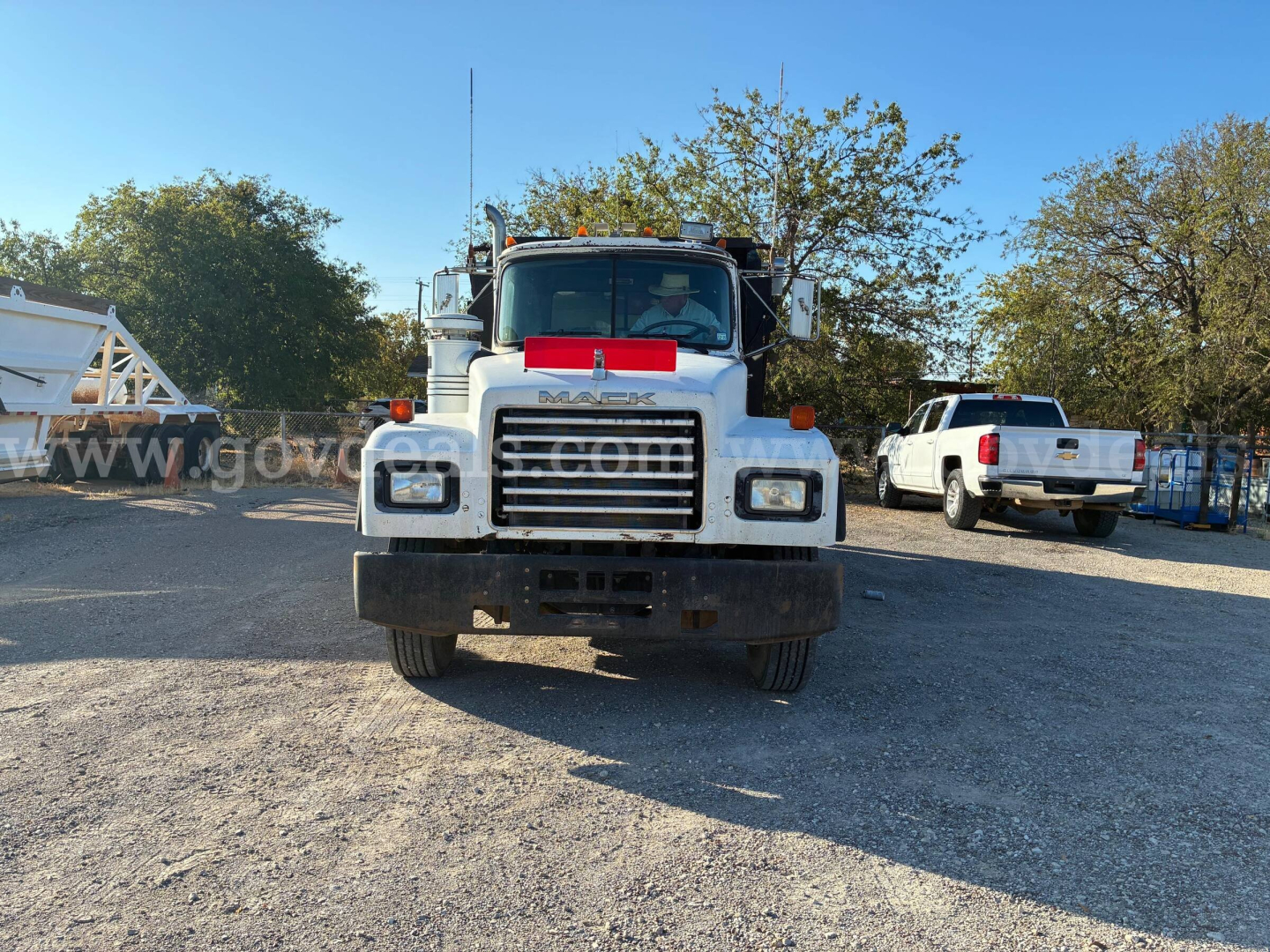 Front view of a white Mack RD690S dump truck with a red reflector band on the hood, large grille, square headlights, and a black bumper.