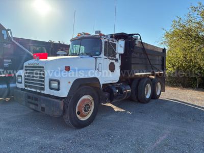 Mack RD dump truck in white with black dump body. Front grille shows MACK logo. Visible text on truck includes 'MACK' on grille and side mirrors. No other legible text clearly readable due to image resolution.