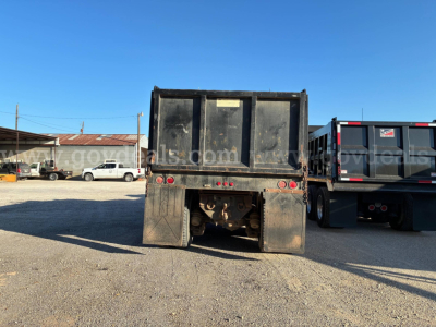 Rear view of a used Mack dump truck RD690S with a black dump bed and dual rear wheels, showing tail lights and mud flaps.