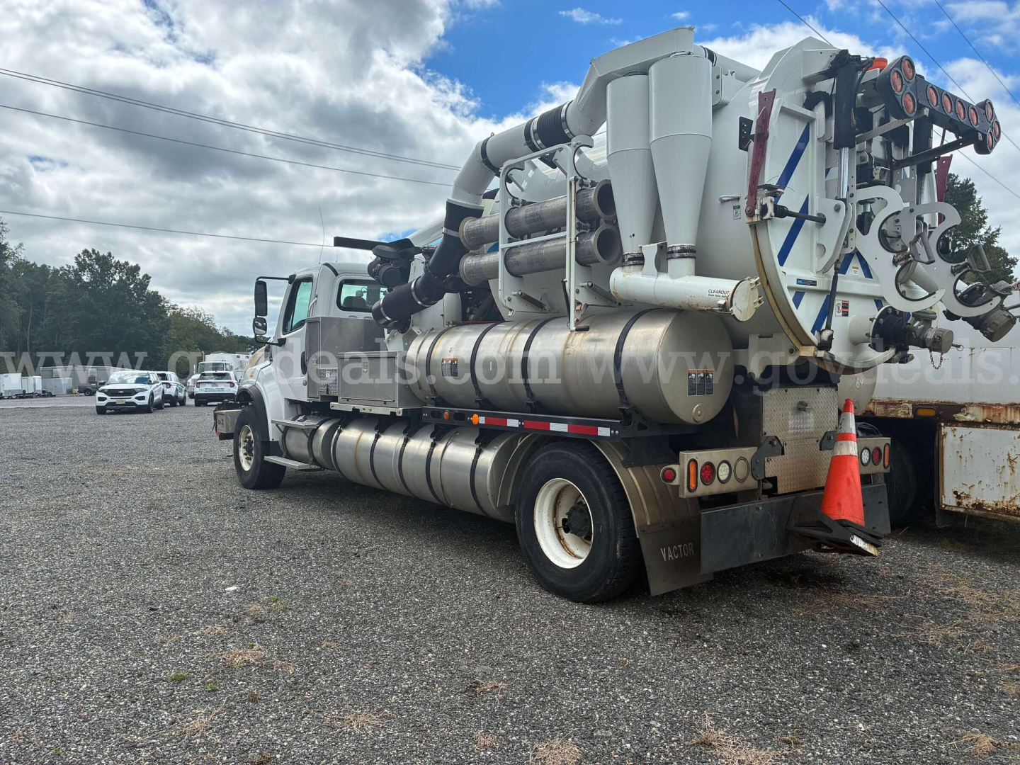 Freightliner M2 106 vacuum truck with large stainless tank and vacuum system mounted behind cab, side view showing rear equipment and hoses.