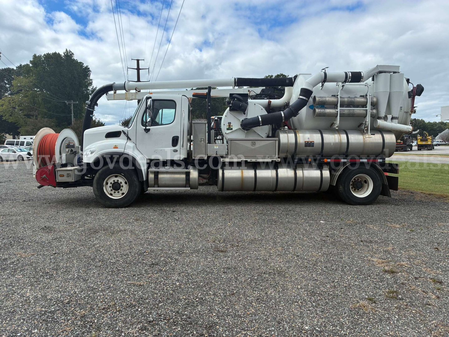 Freightliner M2 106 vacuum truck side view showing large vacuum hoses and stainless steel tanks with rear auger and machinery.