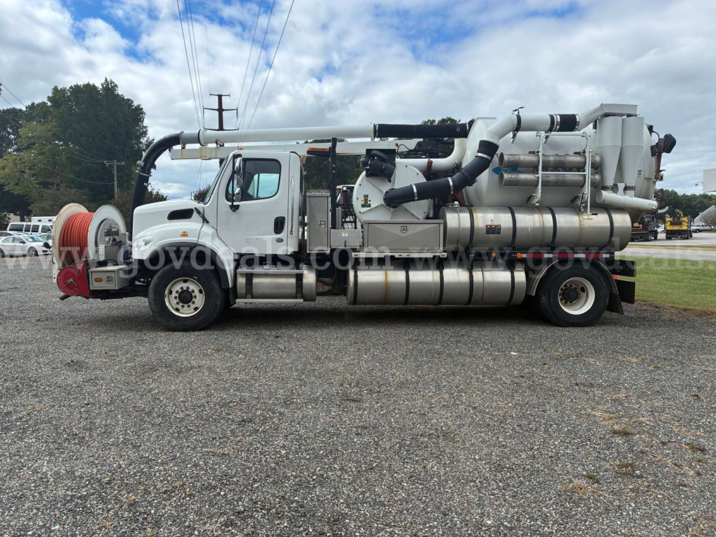 Freightliner M2 106 vacuum truck side view showing large vacuum hoses and stainless steel tanks with rear auger and machinery.