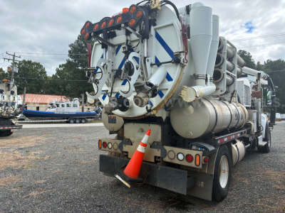 Truck rear view showing vacuum equipment and hoses on a Freightliner M2 106. Visible components include large vacuum tank, hose reels, rear lights, hazard cone, and mounting framework.