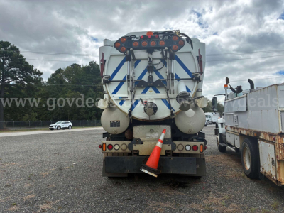 Truck rear view of a Freightliner M2 106 vacuum service vehicle with large water tank, hoses, safety cones, and rear-mounted equipment.