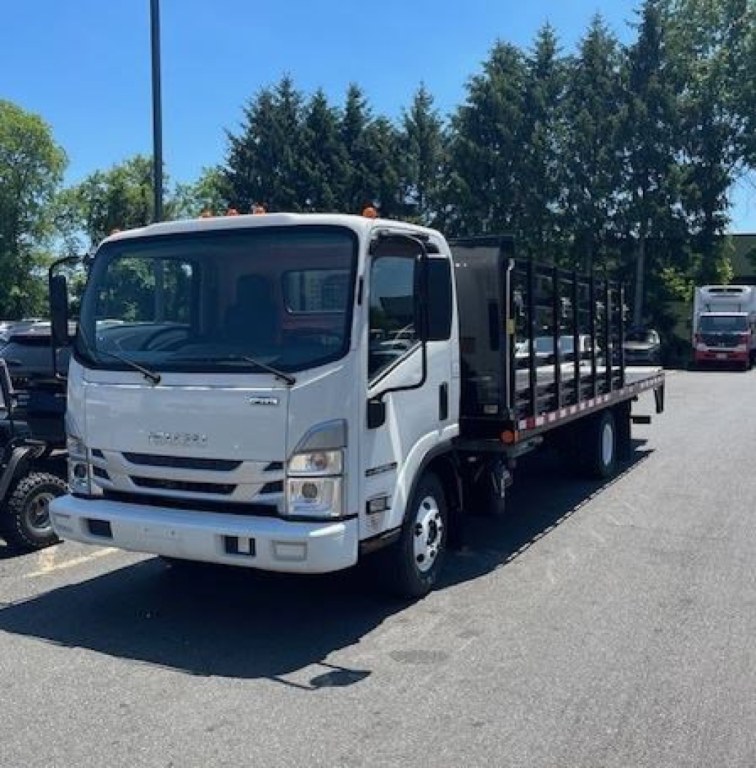 Isuzu NPR HD box truck with white cab, black flatbed cargo area, front grille showing Isuzu emblem. Visible text on front: likely 'ISUZU' and model details; no legible stickers or serials seen.