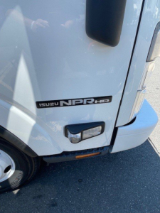 Isuzu NPR HD badge and front corner of box truck showing headlight, bumper, and side marker.