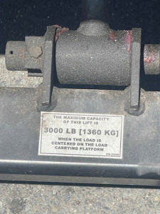 Isuzu NPR HD truck cargo area showing a load rating plate reading 'THE MAXIMUM CAPACITY OF THIS LIFT IS 3000 LB [1360 KG] WHEN THE LOAD IS CENTERED ON THE LOAD CARRYING PLATFORM'