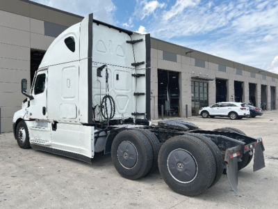 Freightliner Cascadia126 tractor-trailer chassis rear view showing third axle and dual rear wheels, white paint, in-service condition.