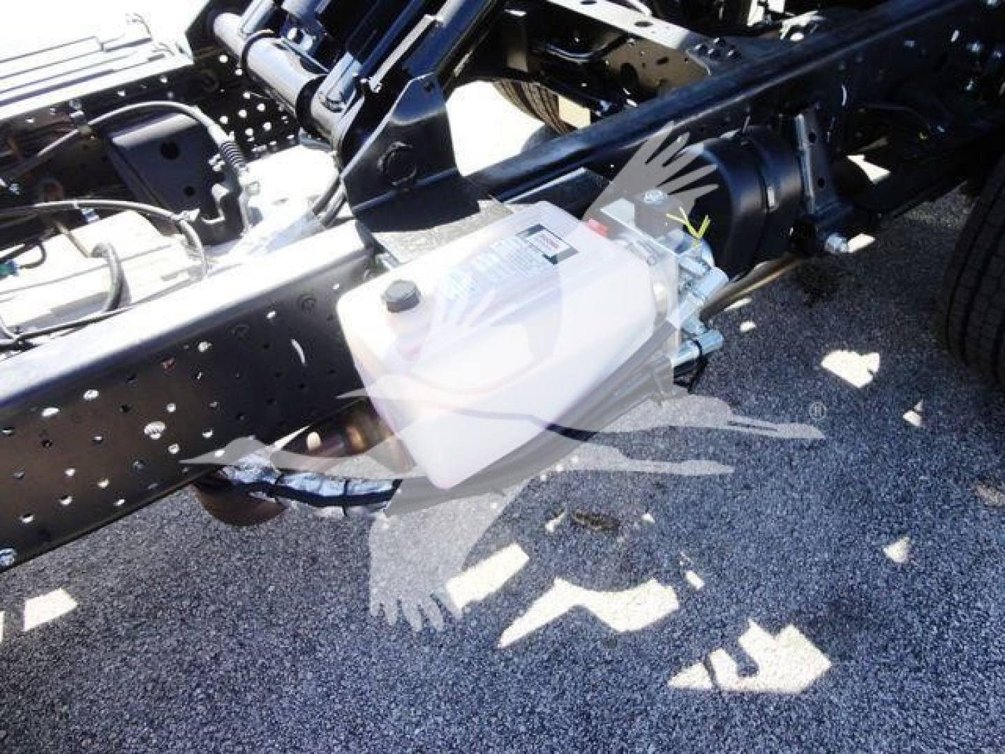 Isuzu NPR HD truck chassis with white auxiliary reservoir mounted near frame, showing hydraulic lines and engine area.