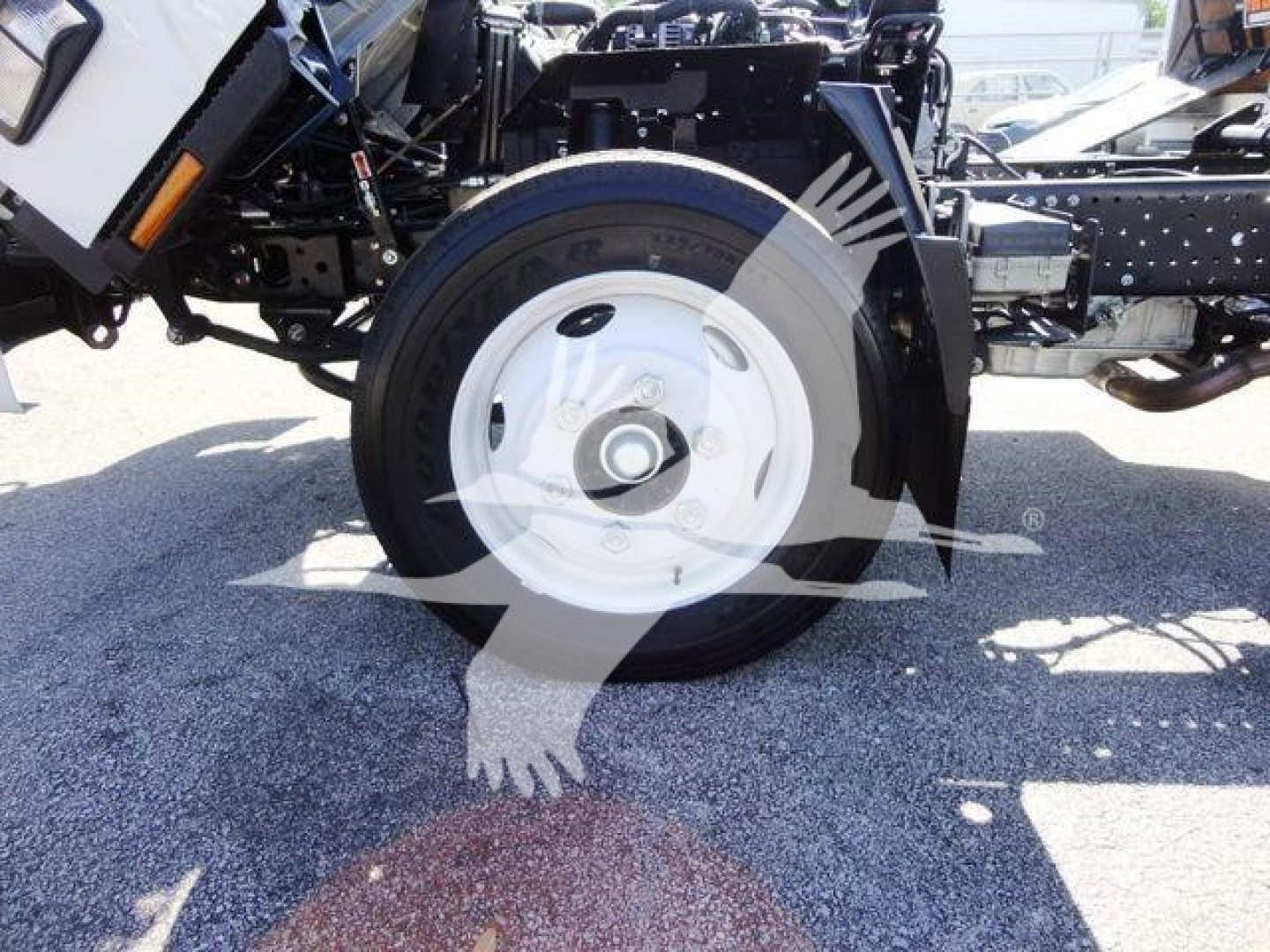 Isuzu NPR-HD truck front wheel and suspension showing white steel wheel and tire, partial chassis, and hydraulic lines.