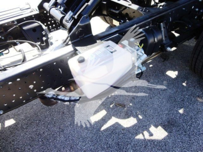 Isuzu NPR HD truck chassis with white auxiliary reservoir mounted near frame, showing hydraulic lines and engine area.