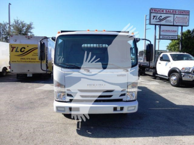 Isuzu NPRHD dump truck front view with TLC Trucks Sales Center signage in background and other equipment nearby.