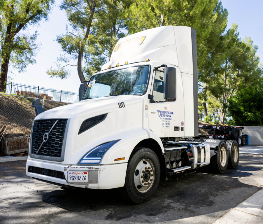 Truck cab of a white 2022 Volvo VNR with sleeper, front grille, and wheel, showing VIN and dealer text on door, side view.