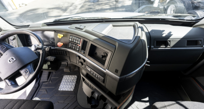 Truck cab interior showing steering wheel, dashboard, and center console of a Volvo VNR, with control panel and gray upholstery.