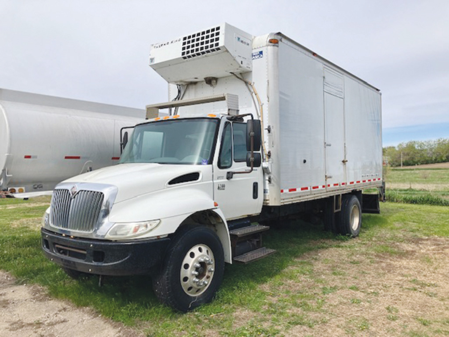 International 4300 refrigerated truck with front cab and reefer unit on top, white box body, California parked on grass.