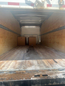 Truck box interior showing empty cargo area with wooden sidewalls and two wooden crates near the far end.