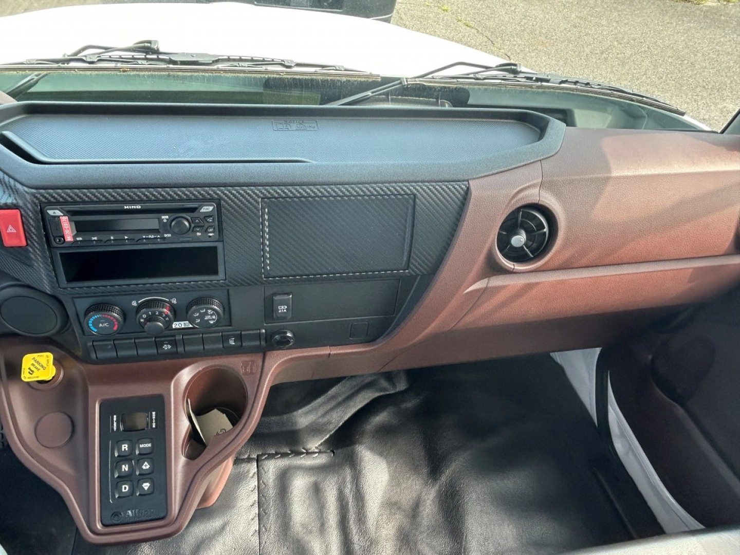 Cab interior of 2025 Hino L6 showing dashboard with radio, climate controls, cup holder, and gear shifter area.