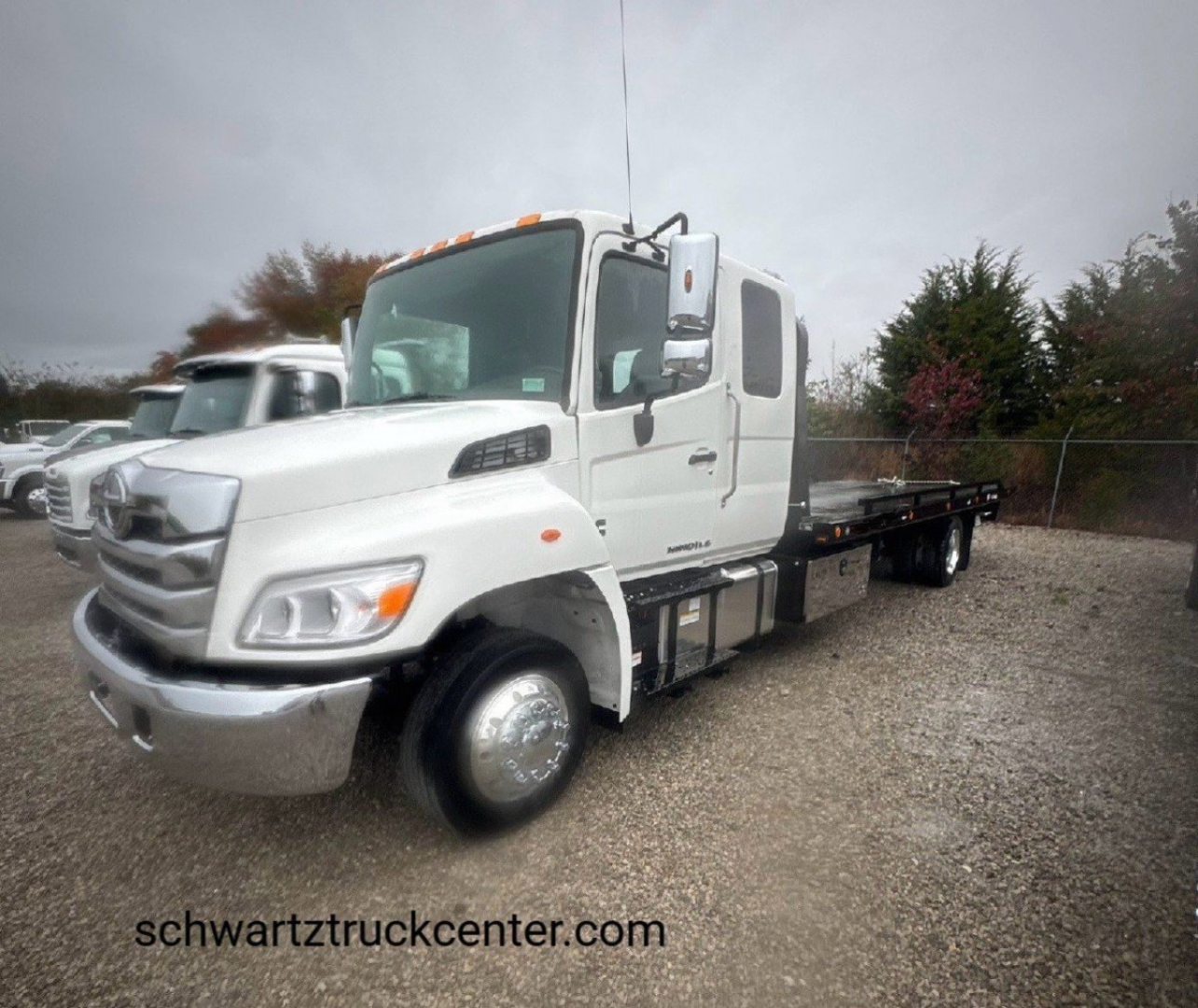 Tow truck showing a white 2025 Hino L6 with flatbed, front grille, and dual rear axles.