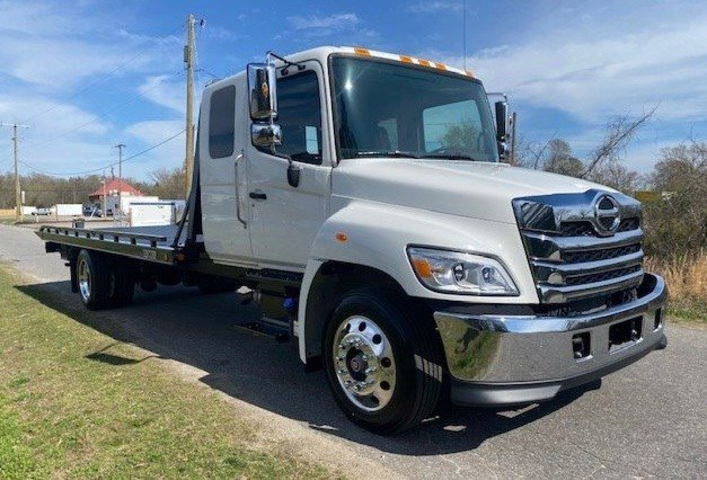 Tow truck front three-quarter view showing cab and flatbed, white exterior, Hino L6 badge not visible, chrome bumper and grille, dual rear wheels.